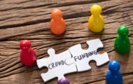 five figurings on the table placed around two pieces of a puzzle that have the words "crowd funding"