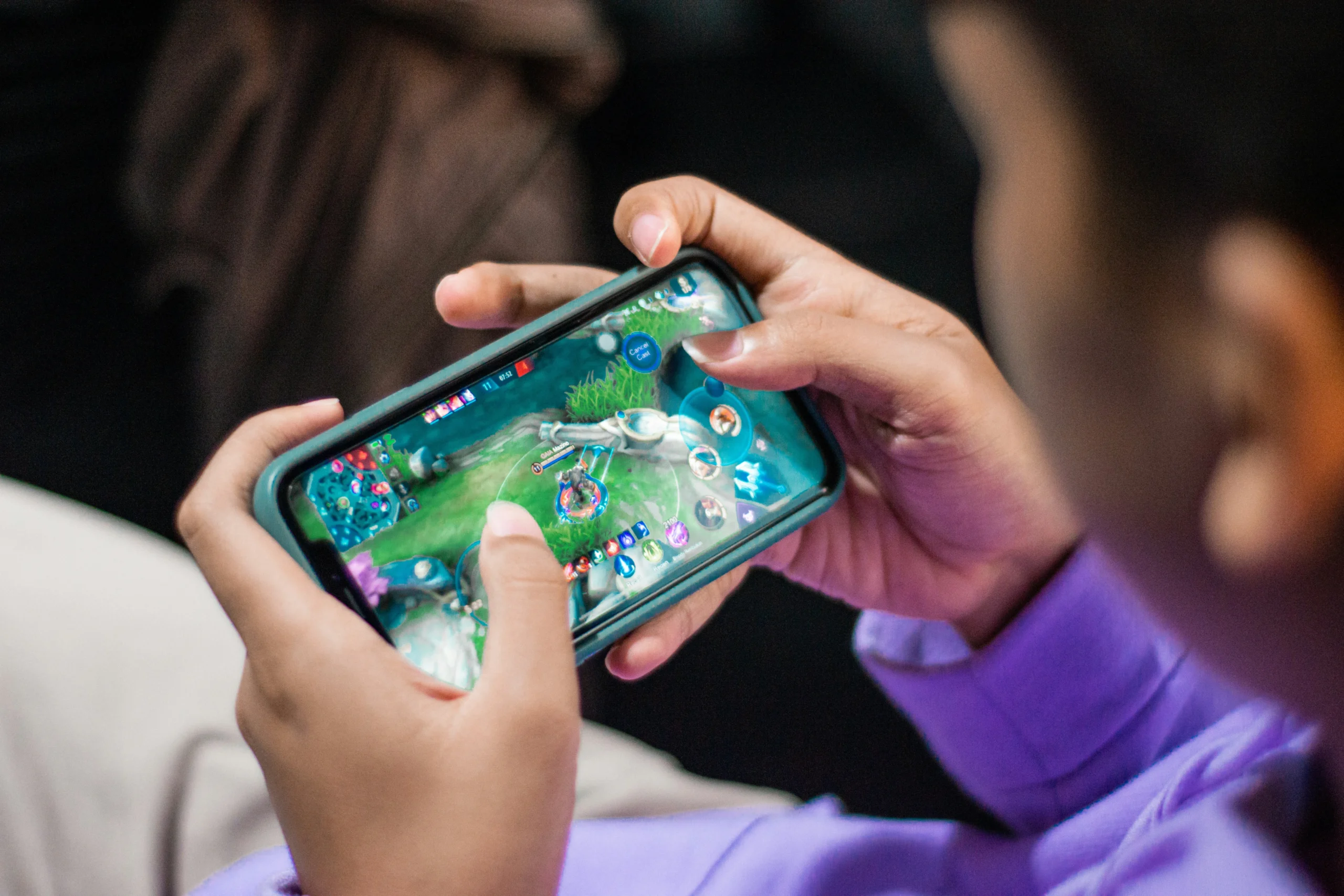 Person playing a mobile multiplayer game on a smartphone held horizontally.